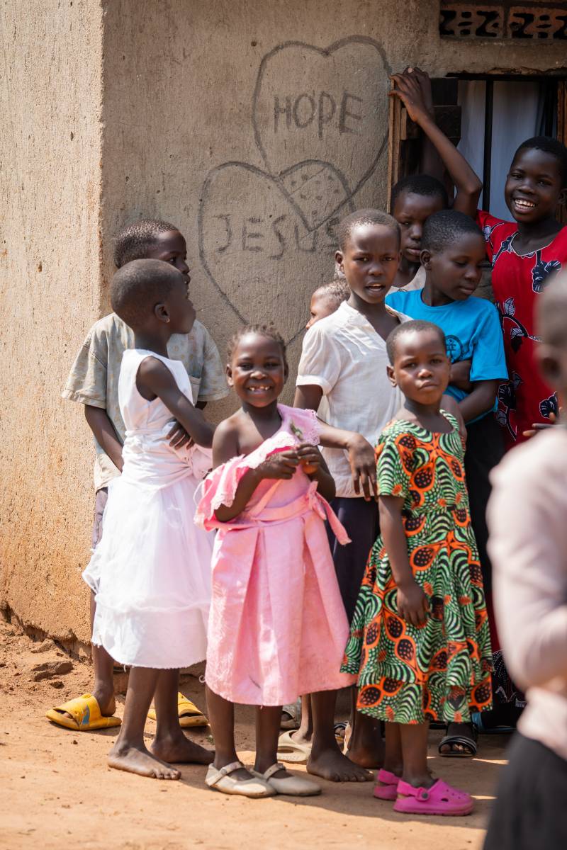 Group of Ugandan kids smiling with the words 'Hope' and 'Jesus' written on the wall behind them.